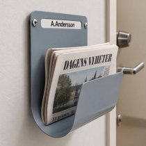 Tidningshållare Lupus med namnskylt bredvid lägenhetsdörr i trapphus